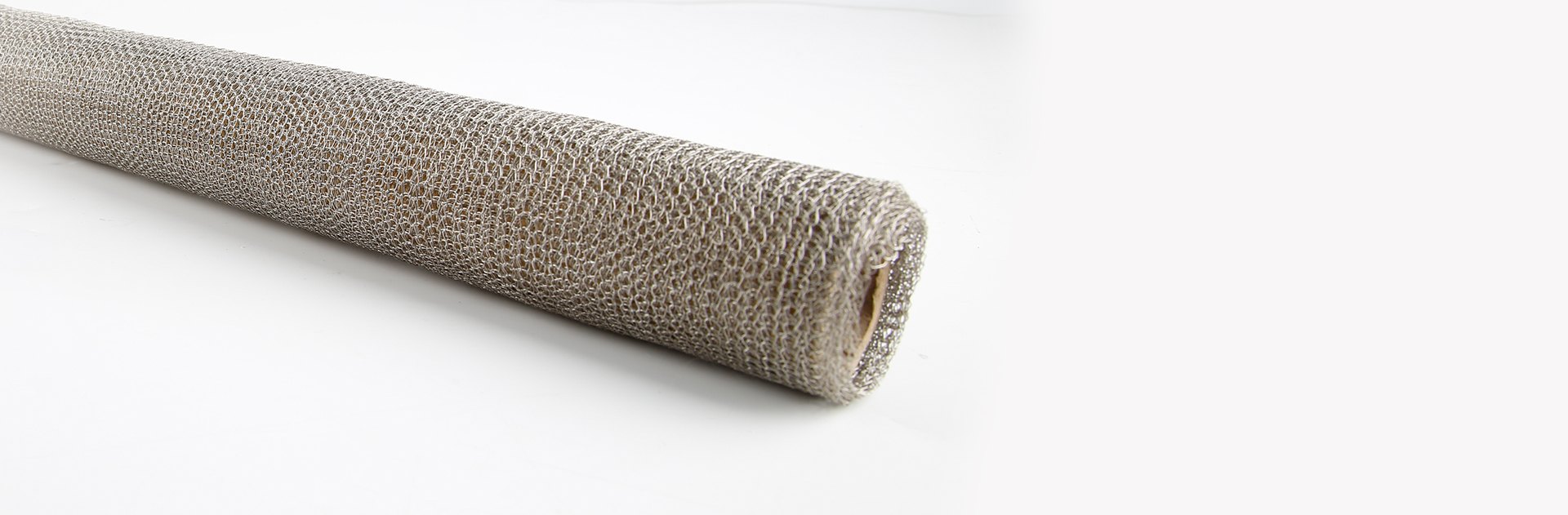 A roll of stainless steel knitted mesh fabric with a metal coin on its stretching part is on the floor.