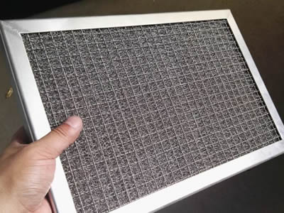 A hand is holding a knitted wire mesh panel with crimped wire mesh grilles.