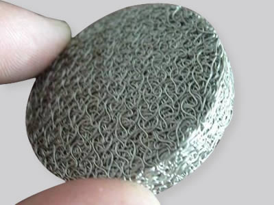 A hand is holding a round wire compressed knitted mesh.