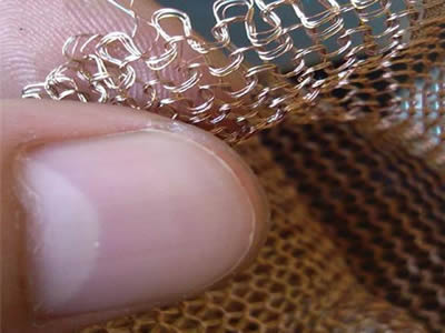 A hand is holding a multi-filament copper knitted mesh.