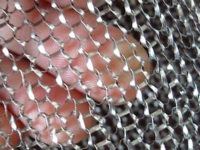 A hand is holding a piece of flat wire knitted mesh fabric.