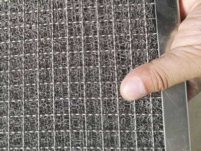 A hand is holding a round wire knitted wire mesh panel.