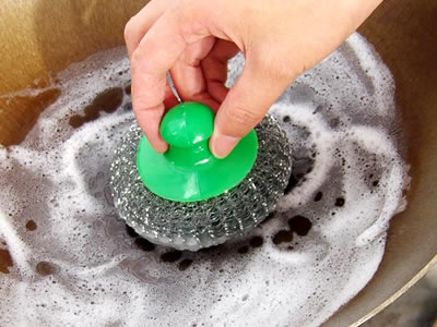 一隻手正在用針織清潔球清潔平底鍋。