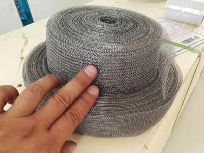 A hand is holding two rolls of knitted wire mesh tapes.
