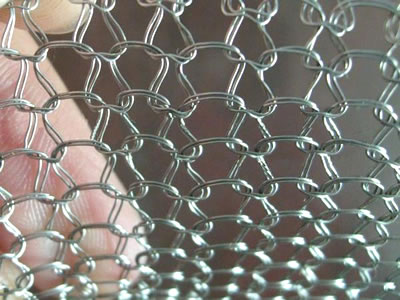 A hand is holding a multi-filament stainless steel knitted mesh.